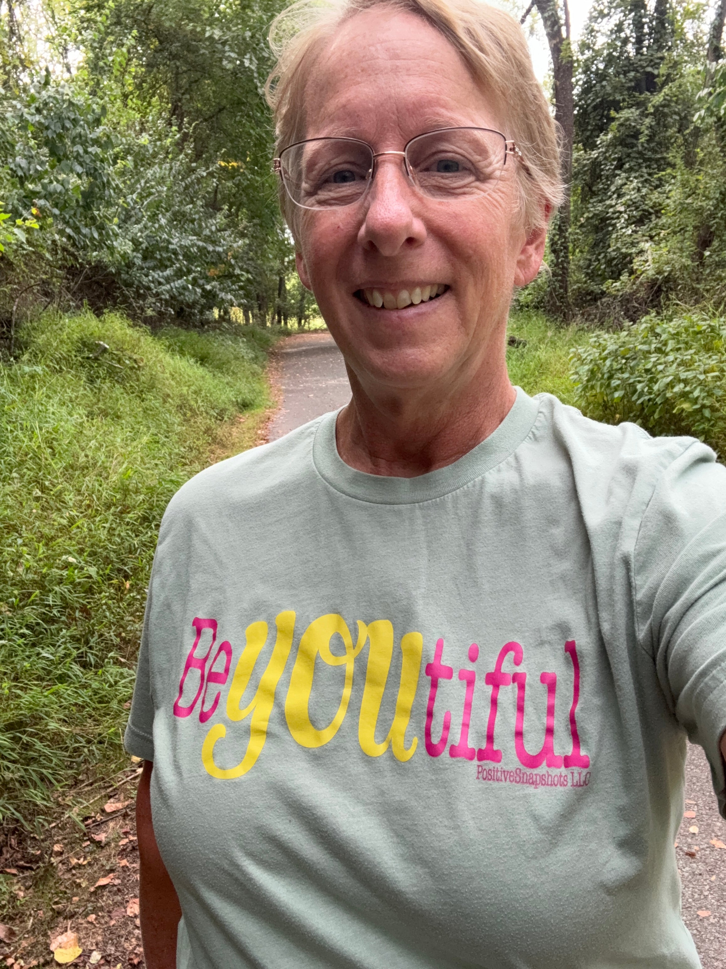 Person wearing a gray sweatshirt with 'be you tiful' text outdoors.