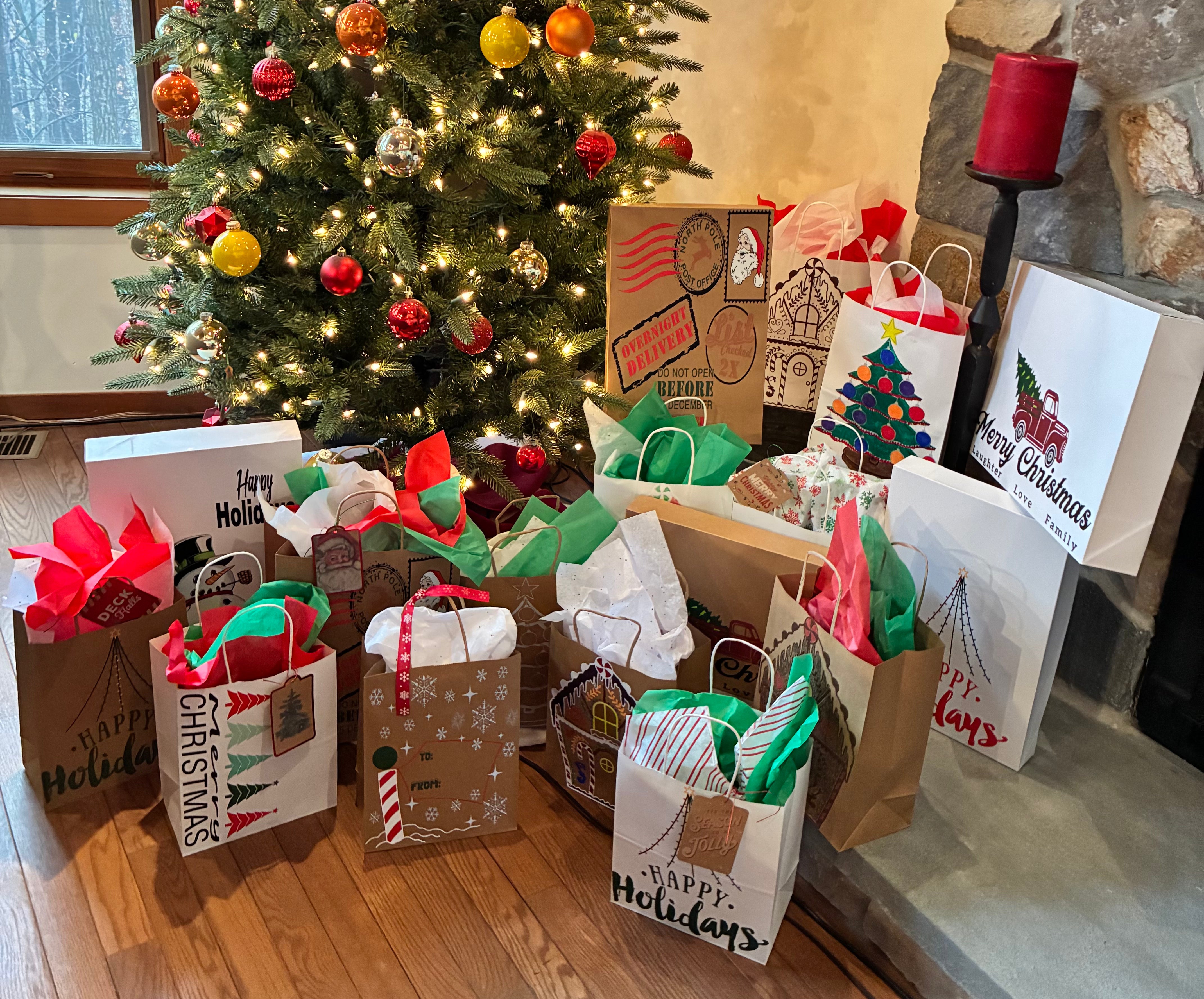 Gift bags with holiday designs in front of a decorated Christmas tree.