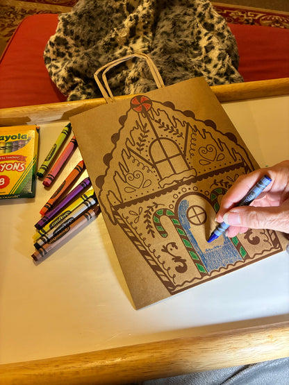 Person coloring a goningerbread house with crayons on a table.